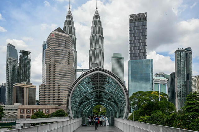 Para turis berfoto dengan Menara Kembar Petronas Malaysia di latar belakang di Kuala Lumpur (15/7/2025). Foto: Mohd Rasfan/AFP