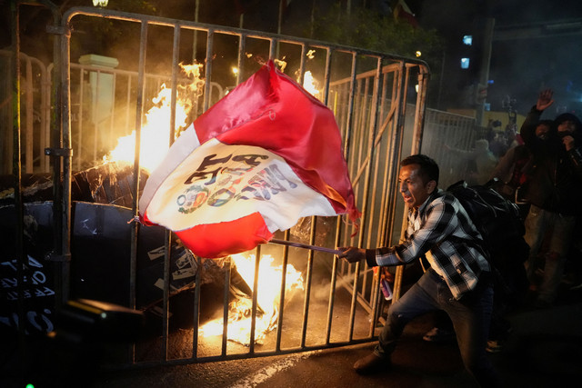 Seorang demonstran mengibarkan bendera Peru di samping api unggun saat mahasiswa, pekerja serikat, dan anggota kelompok sipil dan politik melakukan protes di Lima, Peru, Rabu (15/10/2025). Foto: Angela Ponce/REUTERS