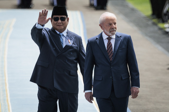 Presiden Prabowo Subianto (kiri) melambaikan tangan saat berjalan bersama Presiden Brazil Luiz Inacio Lula da Silva (kanan) untuk pemeriksaan pasukan di Istana Merdeka, Jakarta, Kamis (23/10/2025). Foto: Yasuyoshi Chiba/AFP