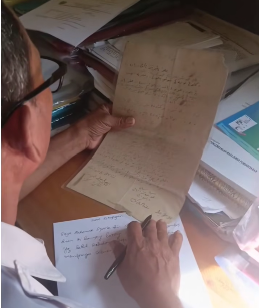 Sekretaris Desa (Sekdes) Merabuan sedang men-transliterasi surat tanah tahun 1938. Foto: Dok. TikTok @sambasinformasi