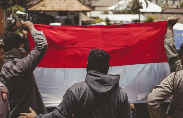 Pria dengan jaket kulit hitam memegang bendera. sumber: unsplash 