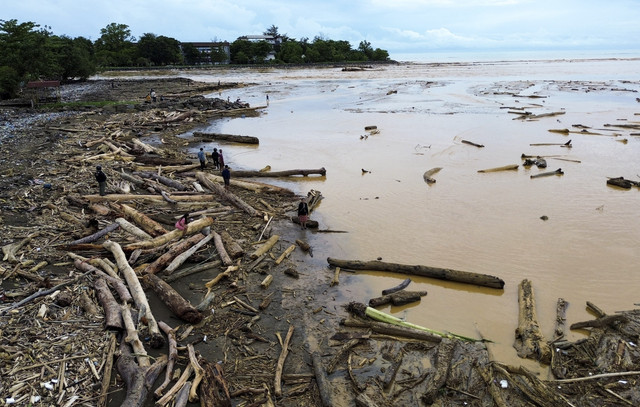 Sejumlah warga berjalan di antara potongan kayu gelondongan yang bertumpuk di pantai Air Tawar, Padang, Sumatera Barat, Jumat (28/11/2025). Foto: Iggoy el Fitra/ANTARA FOTO