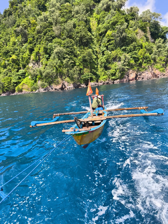Menyusuri birunya laut Pulau Sebesi dengan perahu sederhana, ditemani pemandangan hutan hijau yang masih asri dan alami. Perjalanan ini menghadirkan suasana tenang, di mana laut, daratan, dan kehidupan masyarakat pesisir menyatu dalam keindahan Pulau Sebesi yang apa adanya. (dokumen pribadi)