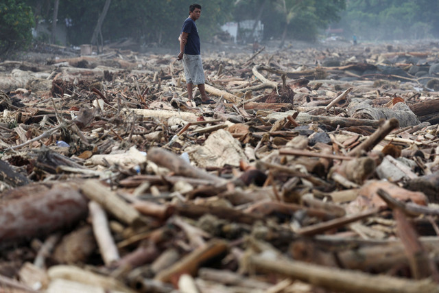 Seorang pria berdiri di tengah batang-batang pohon yang terdampar di pantai setelah banjir bandang dan tanah longsor yang mematikan, di Padang, Provinsi Sumatera Barat, Minggu (30/11/2025). Foto: Willy Kurniawan/REUTERS