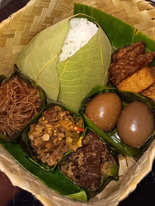 Sego berkat yang dibungkus daun jati disajikan lengkap dengan lauk pauk tradisional seperti telur, tempe, dan tahu bacem, sambal goreng, serta soun. Foto: Sego Berkat Bu Tiwi Tan Tlogo