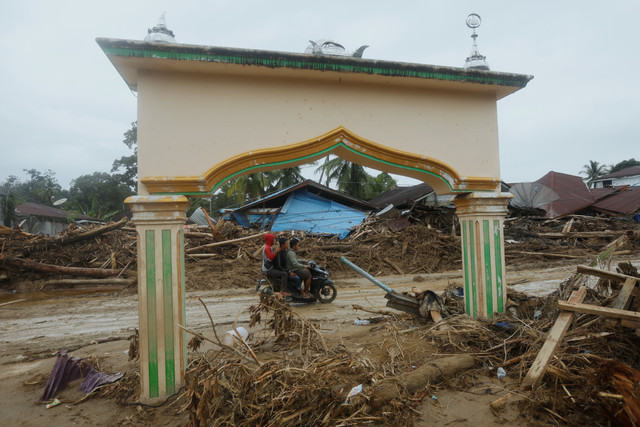 Pengendara motor melewati dekat pohon yang terbawa banjir bandang di Batang Toru, Sumatera Utara, Selasa (2/12/2025).
 Foto: Binsar Bakkara/AP Photo