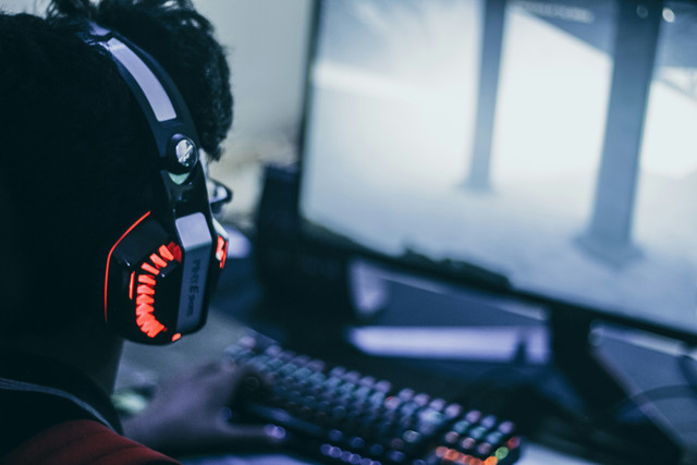 Orang yang sedang duduk dan bermain game menggunakan headphone oranye. Foto: unsplash.com