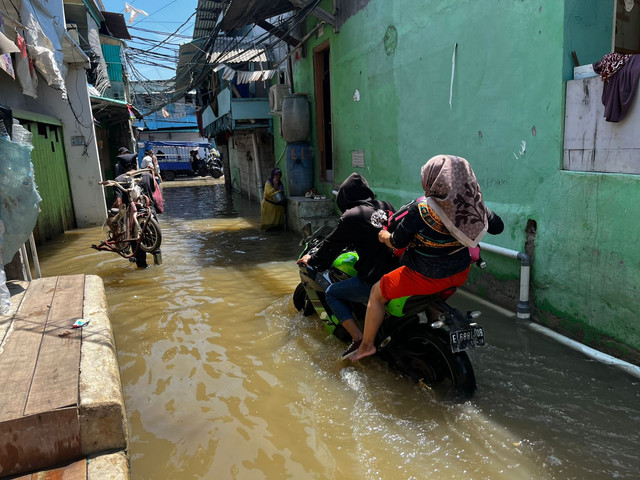 Warga melintasi banjir rob di Jalan Dermaga Ujung, Muara Angke, Jumat (5/12). Foto: Rayyan/Kumparan