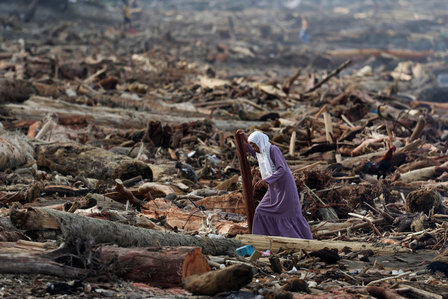 Seorang perempuan berjalan di antara batang-batang pohon yang terdampar di pantai setelah banjir bandang dan tanah longsor yang mematikan, di Padang, Provinsi Sumatera Barat, Minggu (30/11/2025). Foto: Willy Kurniawan/REUTERS sumber. kumparan