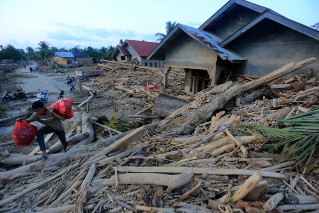 Warga melintasi kayu gelondongan yang terbawa arus banjir di Desa Geudumbak, Kecamatan Langkahan, Aceh Utara, Aceh, Jumat (5/12/2025). Foto: Syifa Yulinnas/ANTARA FOTO