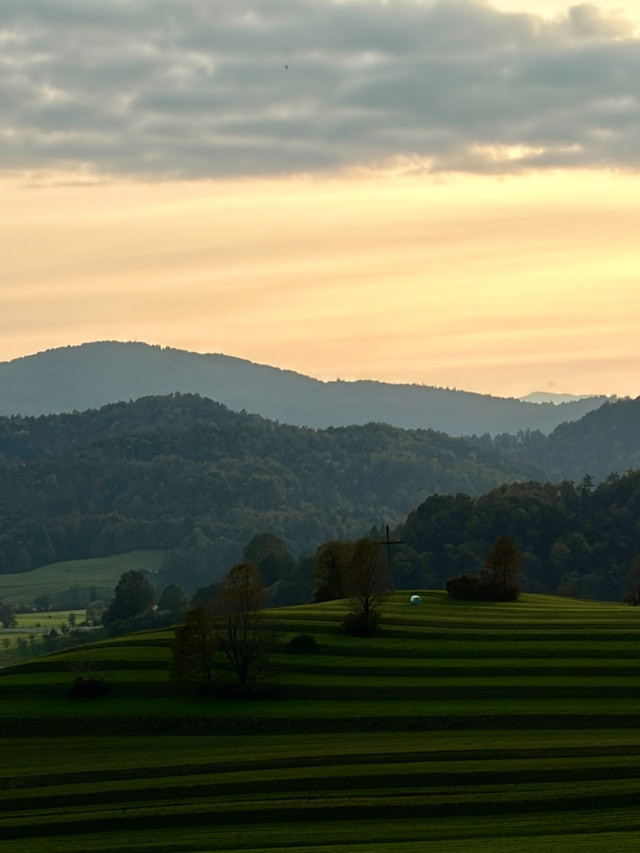 Bukit-bukit hijau yang bergelombang di bawah langit senja yang berawan, Foto Alessio Patron via https://unsplash.com/@alessiop