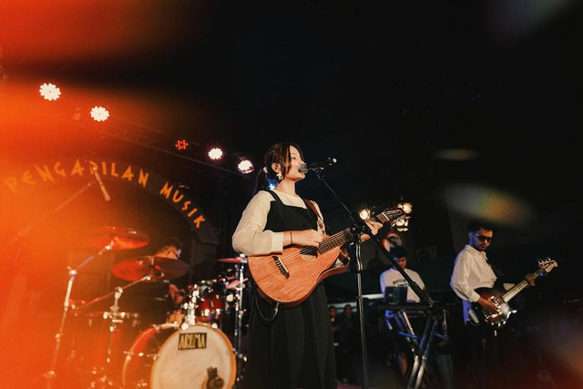 Musisi Aruma pakai gitar dari rotan buatannya saat manggung. Foto: Instagram @arumands