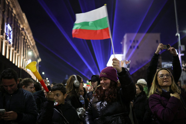 Seorang demonstran mengibarkan bendera Bulgaria saat orang-orang berdemonstrasi di luar gedung parlemen selama unjuk rasa anti-pemerintah, di Sofia, Bulgaria, Rabu (10/12/2025). Foto: Spasiyana Sergieva/REUTERS