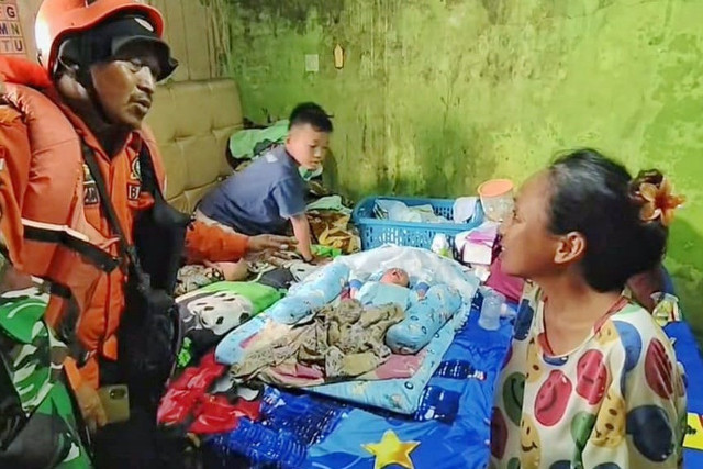 Megawati (kanan) dan bayinya saat akan dievakuasi oleh petugas BPBD Kabupaten Cirebon dan TNI dari rumahnya yang terendam banjir, Senin (15/12/2025). Foto: kumparan