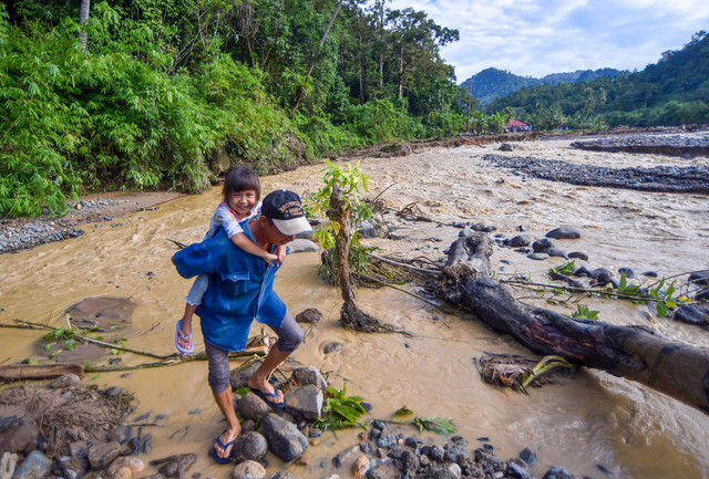 Warga melewati aliran air sungai yang memutus jalan di kawasan Batu Busuk, Pauh, Padang, Sumatera Barat, Selasa (16/12/2025). Foto: ANTARA FOTO/Iggoy el Fitra