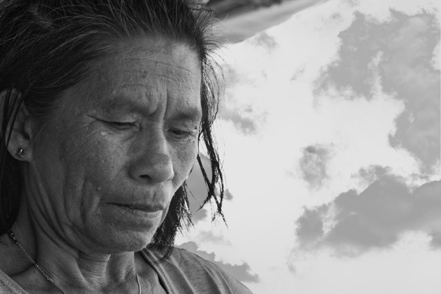 Elderly female preparing food outside canopy in Philippines