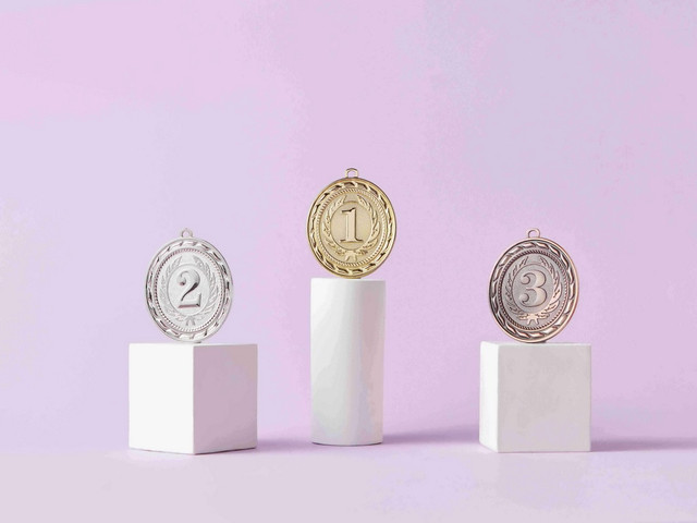 Photo by DS stories: https://www.pexels.com/photo/medals-on-pedestal-on-pink-studio-background-7267588/