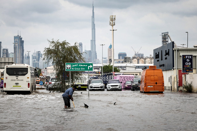 Warga membersihkan saluran air yang tersumbat di jalan yang tergenang banjir di Dubai, Jumat (19/12/2025). Foto: FADEL SENNA / AFP