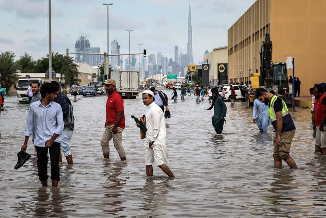 Warga berjalan melewati jalan yang tergenang banjir di Dubai, Jumat (19/12/2025). Foto: FADEL SENNA / AFP
