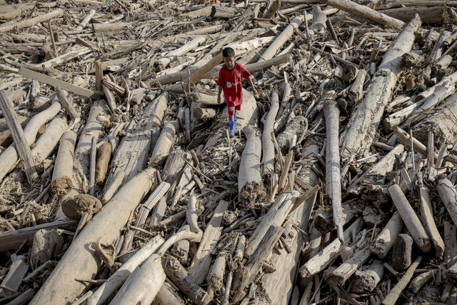 Seorang bocah berjalan meniti kayu-kayu yang memenuhi kawasan pascabanjir bandang di Desa Kota Lintang Bawah, Kecamatan Kuala Simpang, Kabupaten Aceh Tamiang, Aceh, Senin (22/12/2025). Foto: Jamal Ramadhan/kumparan