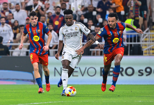Vinicius Junior (tengah) dikejar Pedri (kiri) dan Jules Kounde (kanan) dalam laga Barcelona vs Real Madrid saat Final Piala Super Spanyol 2026 di King Abdullah Sports City Stadium, Jeddah, Arab Saudi, pada Senin (12/1) dini hari WIB. Foto: REUTERS/Stringer