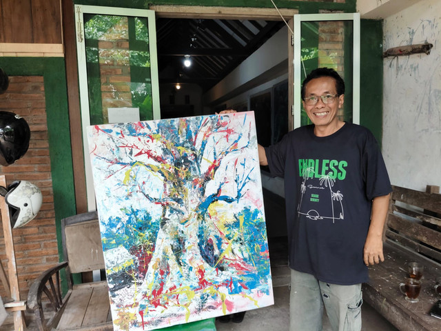 Seorang seniman bernama Hatmojo melukis pohon randu alas raksasa di Desa Tuksongo, Kecamatan Borobudur, Kabupaten Magelang. Foto: Arfiansyah Panji/kumparan