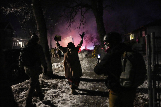 Seorang demonstran mengangkat tangannya sambil berjalan di pinggir jalan dekat petugas penegak hukum, saat ketegangan meningkat di Minneapolis utara, Minnesota, AS, Rabu (15/1/2026). Foto: Leah Millis/REUTERS