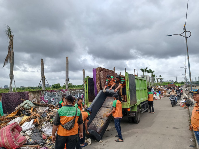 Petugas Dinas Lingkungan Hidup Jakarta Barat mengerahkan tujuh mobil pengangkut sampah untuk mengangkut sampah yang berserakan di Kembangan Baru, Jakarta Barat di samping Kali Mookervart pada Senin (26/1).  Foto: Ryan Iqbal/kumparan