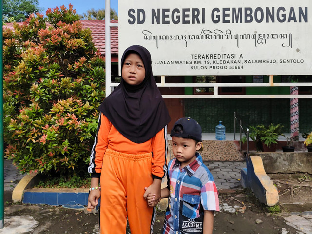 Ariendra Ralea Irgantari (9) ke sekolah membawa adiknya, Reyfan Elcaraka Fahturohman (4), di SD Negeri Gembongan, Kalurahan Salamrejo, Kapanewon Sentolo, Kabupaten Kulon Progo, Rabu (28/1). Foto: Arfiansyah Panji/kumparan