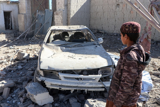 Anak-anak Afghanistan berjalan melewati mobil yang rusak setelah serangan udara Pakistan di desa Balish, distrik Urgun, Provinsi Paktika, Pakistan, pada Februari lalu. Foto: AFP
