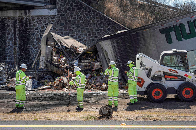 Para pekerja berdiri di samping puing-puing trailer yang digunakan untuk memblokir jalan raya setelah serangkaian blokade dan serangan oleh kejahatan terorganisir menyusul operasi militer di mana bos kartel Nemesio Oseguera, "El Mencho," tewas. Foto: REUTERS/Ivan Arias
