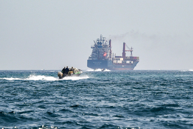 Sebuah perahu mendekati kapal kontainer Marsa Victory berbendera St Kitts dan Nevis saat berlayar di perairan Selat Hormuz di lepas pantai Khasab di semenanjung Musandam utara Oman pada 25 Juni 2025. Foto: Giuseppe Cacace/AFP