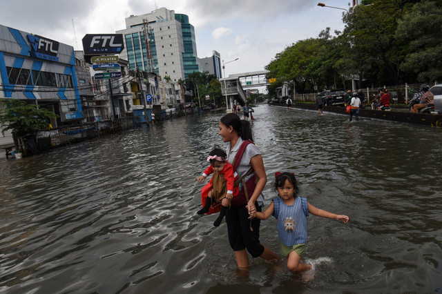 Seorang ibu bersama dua anaknya melintasi genangan banjir di kawasan Green Garden, Jalan Panjang, Jakarta, Minggu (8/3/2026). Foto: Indrianto Eko Suwarso/ANTARA FOTO