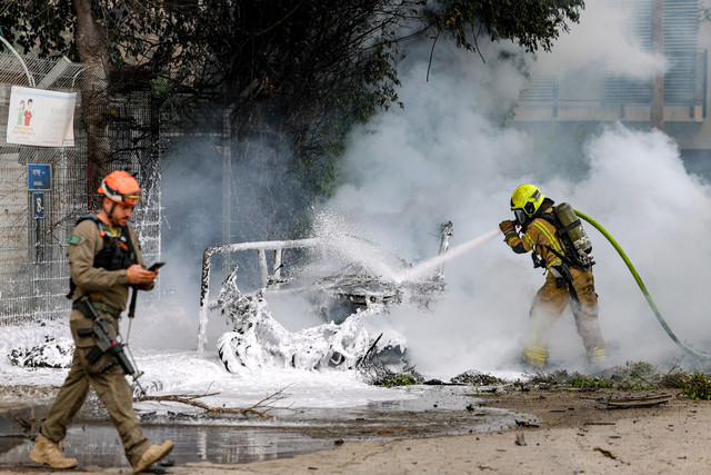 Petugas pemadam kebakaran memadamkan api di dalam kendaraan setelah terkena dampak proyektil dari serangan Iran di Tel Aviv, Minggu (15/3/2026). Foto: JACK GUEZ / AFP
