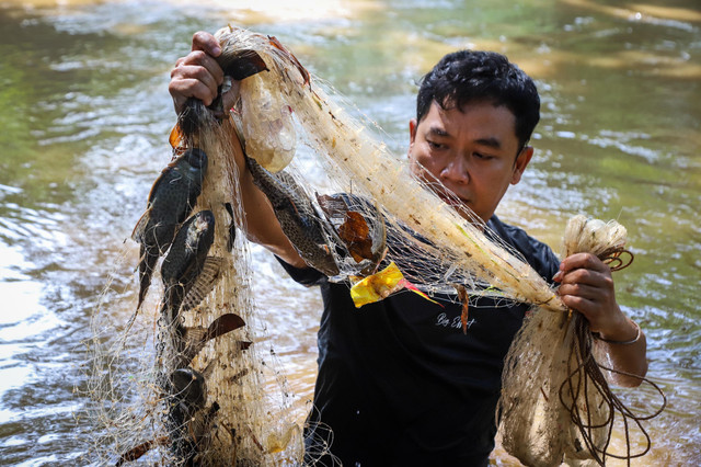 Seorang konten kreator menjaring ikan sapu-sapu di Kali Ciliwung, Jakarta, Senin (6/4/2026). Foto: Iqbal Firdaus/kumparan