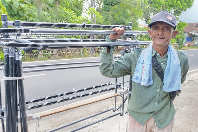 Abdul Rochim (70) membawa dagangannya berupa jemuran baju sambil berjalan kaki. Foto: Vega Ma'arrijil Ula/kumparan