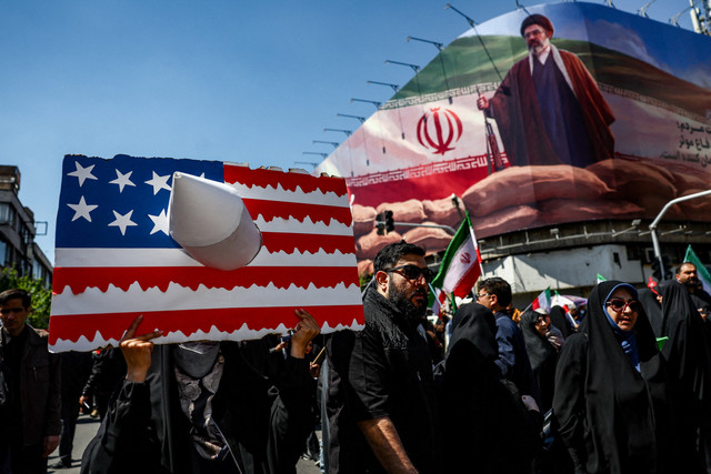 Seseorang memegang plakat yang mewakili bendera AS, dengan gambar Pemimpin Tertinggi Iran yang baru, Mojtaba Khamenei, di papan reklame pada hari upacara peringatan 40 hari wafatnya Ayatollah Ali Khamenei di Teheran, Iran, Kamis (9/4/2026). Foto: Majid Asgaripour/WANA via REUTERS