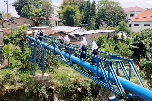 Sejumlah pelajar SMP di Medan menyeberangi sungai dengan menapaki saluran pipa, Kamis (16/4/2026). Foto: Amar Marpaung/kumparan