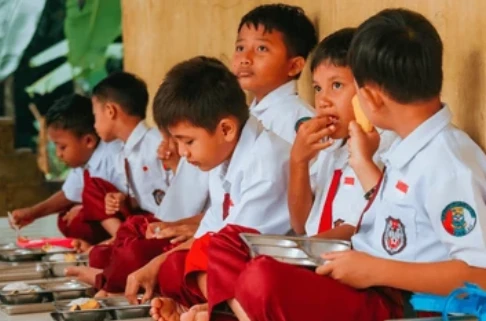 Anak-anak sekolah dasar di Lampung, sedang duduk bersama sambil makan makanan bergizi gratis. Foto: Shutterstock