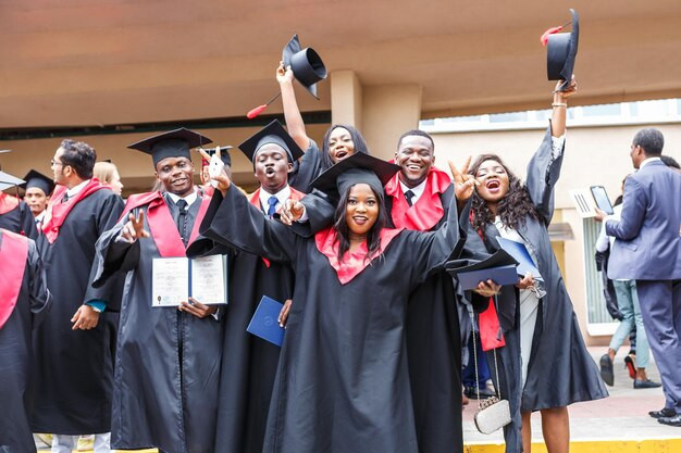 Happy foreign african medical students in square academic graduation caps and black raincoats during commencement with diploms after finishing studies. Photo by: jantsarik/Shutterstock.