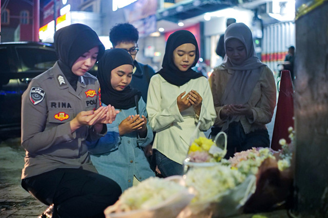 Sejumlah warga tampak berdoa di hadapan karangan bunga sebagai bentuk belasungkawa dan penghormatan terhadap anggota polisi yang tewas ditembak saat menggagalkan curanmor di Lampung Geh, Bandar Lampung. Foto: Dok. Lampung Geh