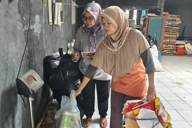 Nasabah Nur (kanan) menyerahkan sampah yang telah dipilah kepada Ketua Bank Sampah Bumi Lestari, Sukini (59), untuk ditimbang dan dihitung nilainya di Srengseng, Jakarta Barat, Minggu (17/5/2026). Foto: Aditya Nugraha/kumparan