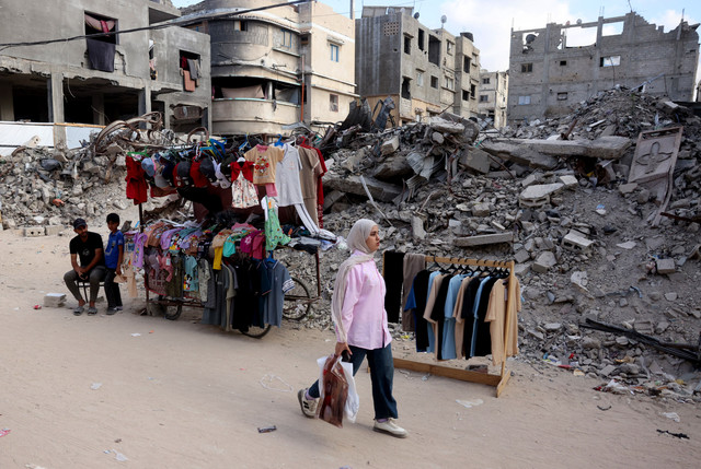 Wanita Palestina berjalan melewati kios pakaian dekat reruntuhan bangunan akibat serangan militer Israel menjelang Idul Adha di Khan Yunis, selatan Jalur Gaza, Selasa (26/5/2026). Foto: Bashar Taleb/AFP
