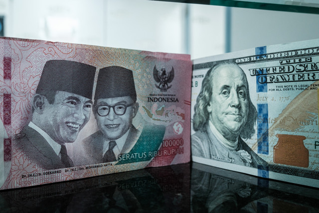 Sejumlah uang kertas pecahan 100.000 rupiah Indonesia difoto di samping uang kertas pecahan 100 dolar AS di sebuah tempat penukaran mata uang di Jakarta, Kamis (4/6/2026). Foto: Yasuyoshi Chiba/AFP