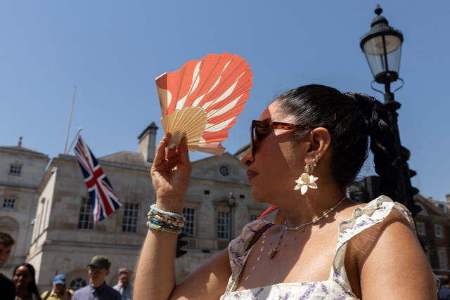Seorang warga menghalau teriknya sengatan matahari menggunakan kipas tangan di pusat kota London, Inggris, Kamis (25/6/2026). Foto: BROOK MITCHELL/AFP