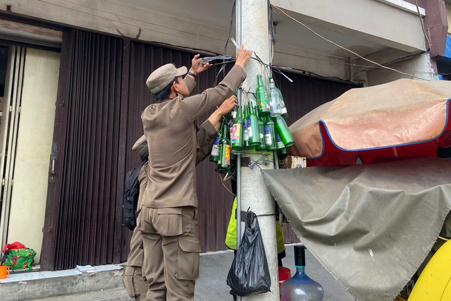 Satpol PP Karawang membersihkan botol-botol miras yang dipasang warga di tiang listrik sebagai bentuk protes. Foto: Satpol PP Karawang