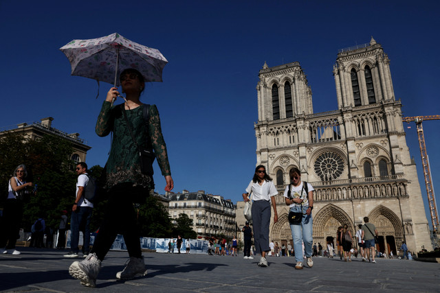 Seseorang berlindung di bawah payung di luar Katedral Notre-Dame di tengah gelombang panas yang hebat di Paris, Prancis, Jumat (26/5/2026). Foto: Tom Nicholson/REUTERS