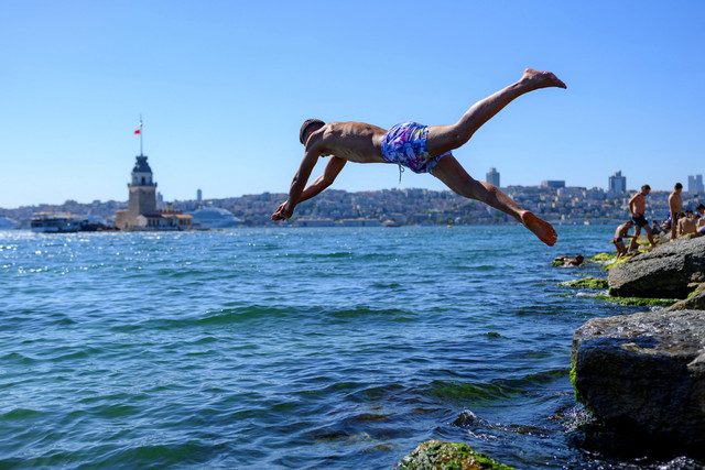 Seorang warga meloncat ke laut saat gelombang panas melanda Istanbul, Turki, Minggu (28/6/2026). Foto: Yasin AKGUL / AFP