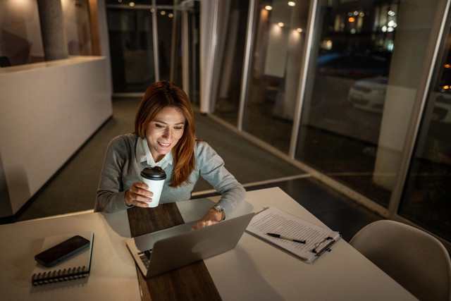 Seorang anak muda bekerja hingga larut malam ditemani laptop dan secangkir kopi. Foto ini merepresentasikan budaya hustle yang sering dikaitkan dengan produktivitas berlebihan dan tekanan untuk selalu sibuk. sumber: unsplash