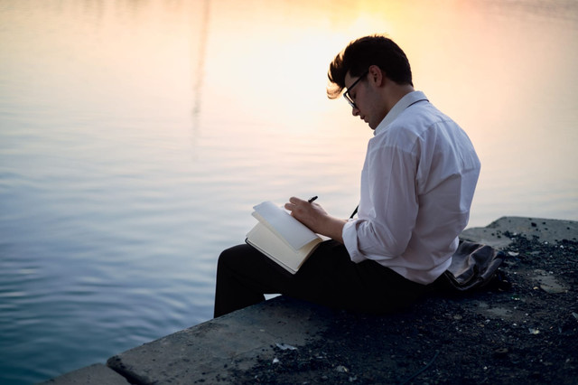 Ilustrasi: Seseorang duduk di tepi danau sambil menulis di buku catatan, merefleksikan kembali mimpi-mimpi yang pernah terlupakan di tengah tuntutan kehidupan. (Sumber:https://www.pexels.com/)
